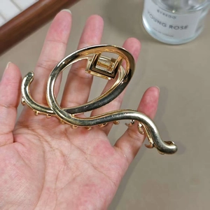 Minimalist gold wave hair claw clip held by hand showing metallic glossy finish