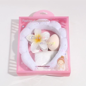 Skincare set with white plush headband, pink makeup sponge, and plumeria flower clip in box