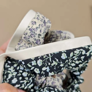 Détail de chouchou en tissu à motif floral noir et bordure en similicuir blanc élégant