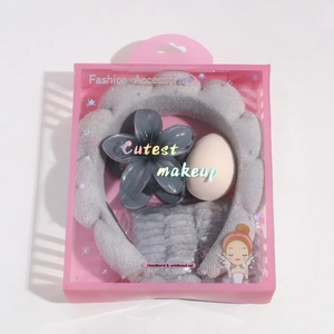 Detailed set featuring grey puffy headband, wristbands, floral clip and makeup sponge in a box
