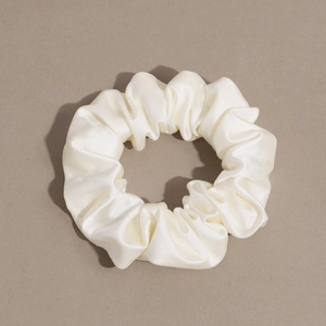 Detail shot of a cream-colored satin scrunchie showing soft fabric texture and elastic design