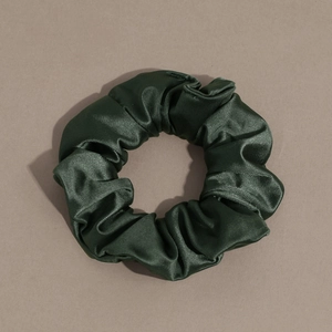 Detailed close-up of dark green satin scrunchie showing smooth pleated silk texture