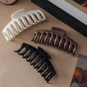 Trois grandes pinces à cheveux mates en beige, marron et noir sur fond de bois clair