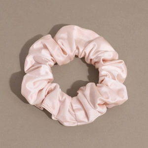 Detail of light pink satin scrunchie showing smooth texture and elegant pleated design