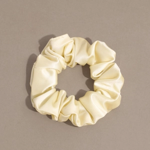 Detailed close-up of cream-colored satin scrunchie showing smooth pleated fabric texture