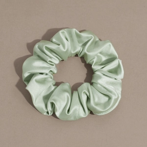 Detailed view of mint green satin scrunchie showing glossy fabric texture and pleats