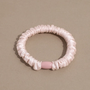 Detailed macro view of light pink satin scrunchie texture with smooth plastic buckle