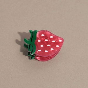 Détail macro d'une pince à cheveux fraise rouge avec finition nacrée et pois blancs