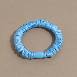 Detail of light blue silk scrunchie featuring soft satin pleats and matching curved clip