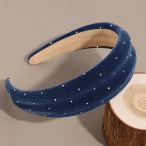 Detailed close-up of dark blue velvet headband with silver studs on wooden block