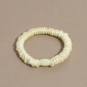 Detailed view of cream yellow satin hair scrunchie with soft pleated fabric and pearl bead