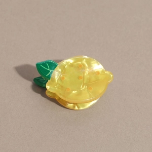 Gros plan d'une pince à cheveux citron jaune avec des poignées en forme de feuilles vertes