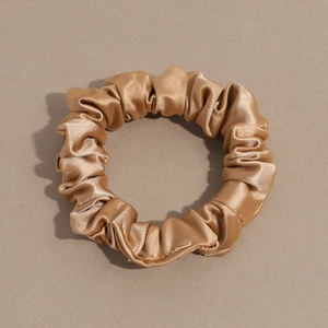 Detail of champagne gold satin scrunchie showing glossy texture and pleated fabric design