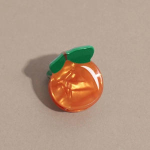 Détail de la pince à cheveux orange avec texture marbrée et petite feuille verte