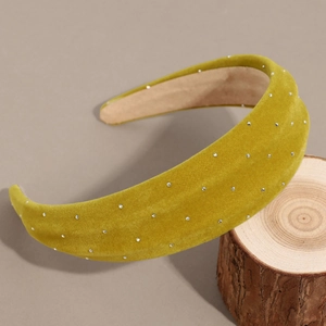 Detail view of mustard yellow velvet headband with silver rhinestones on a wooden stand