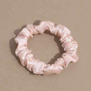Close-up of soft pink satin scrunchie with silky luster and elegant pleated texture