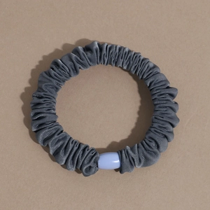 Detail of dark grey satin scrunchie with matte purple oval bead on a neutral background