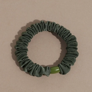 Close-up of dark green scrunchie with soft fabric texture and a polished oval bead