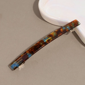 Detailed view of tortoise shell acetate hair clip with gold logo on a ceramic dish
