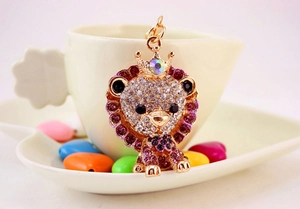 Macro detail of a crystal-studded lion keychain with a crown on a white coffee cup