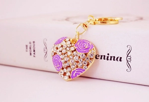 Detail of a heart keychain with purple roses and white rhinestones on golden metal base
