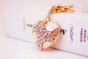 Close-up of heart-shaped keychain with gold alloy, white rose enamel and sparkling rhinestones