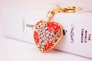 Close-up of heart keychain with red roses and crystals on a white book surface