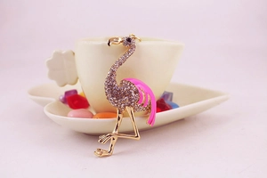 Détail d'un pendentif flamant rose doré serti de cristaux posé sur une tasse à café