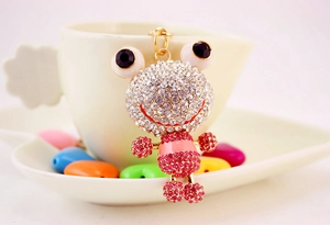 Détail d'un porte-clés grenouille en strass avec accents roses suspendu à une tasse blanche