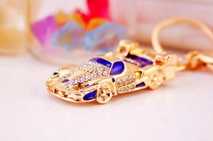 Macro shot of gold-plated metal sports car keychain with blue enamel and sparkling rhinestones