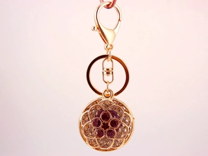 Detailed view of a gold-plated flower keychain with purple and clear crystals