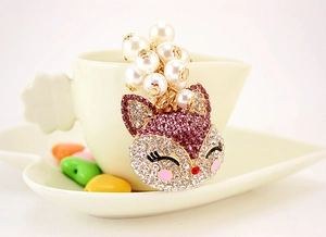 Detail of fox-shaped keychain with purple crystals and white faux pearls on golden base