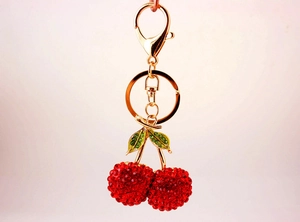 Close-up of sparkling red rhinestone cherry keychain with green leaves and gold clasp
