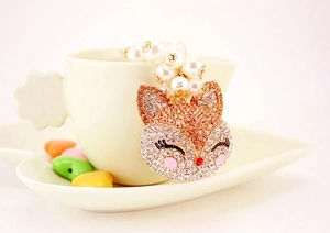 Detail of fox head keychain with rhinestones, faux pearl chain on a white cup