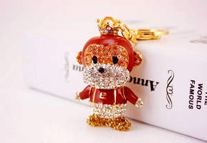 Detailed close-up of a crystal monkey keychain with red enamel and gold crown on a book