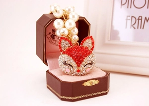 Macro detail of fox head keychain with faux pearls and red rhinestones in a gift box