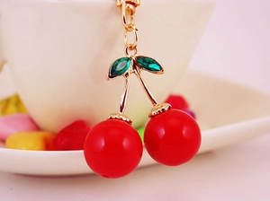 Gros plan d'un porte-clés cerise rouge avec tige dorée et feuilles en cristal vert