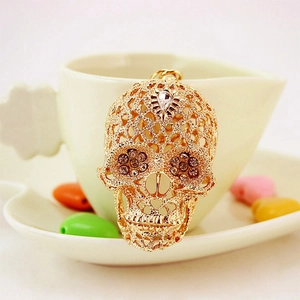 Golden skull keychain with hollow floral pattern and crystal eyes on a white porcelain cup