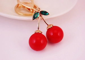 Gros plan sur un porte-clés cerise rouge avec feuilles en cristal et fermoir doré