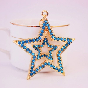 Double-layered star keychain with blue rhinestones and gold metal hanging on a white cup