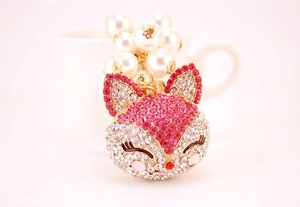 Close-up of pink rhinestone fox keychain with white pearls on a gold metal base
