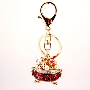 Golden keychain with a miniature red enamel incense burner and white faux pearls