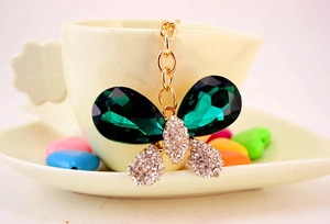 Détail du porte-clés papillon en cristal émeraude accroché à une tasse avec chaîne dorée