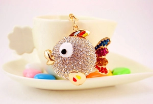 Dettaglio di un portachiavi a forma di pesce con cristalli e pinne arcobaleno su una tazza