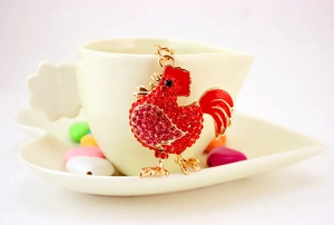 Dettaglio portachiavi a forma di gallo con strass rossi e smalto su piatto in ceramica