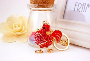 Dettaglio portachiavi a forma di gallo dorato con strass rossi e finitura smaltata
