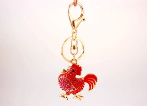 Dettaglio portachiavi a forma di gallo dorato con strass rossi e rifiniture in smalto
