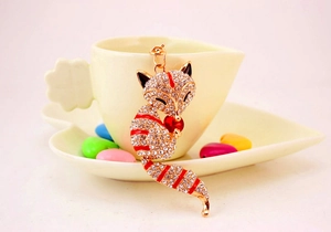 Detail of crystal fox keychain with red gemstone on a ceramic cup edge