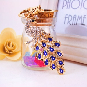 Peacock keychain in gold metal with rhinestones and blue evil eye charms hanging on a bottle