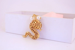 Close-up of golden snake pendant with heart cut-outs and pearl accents on white box